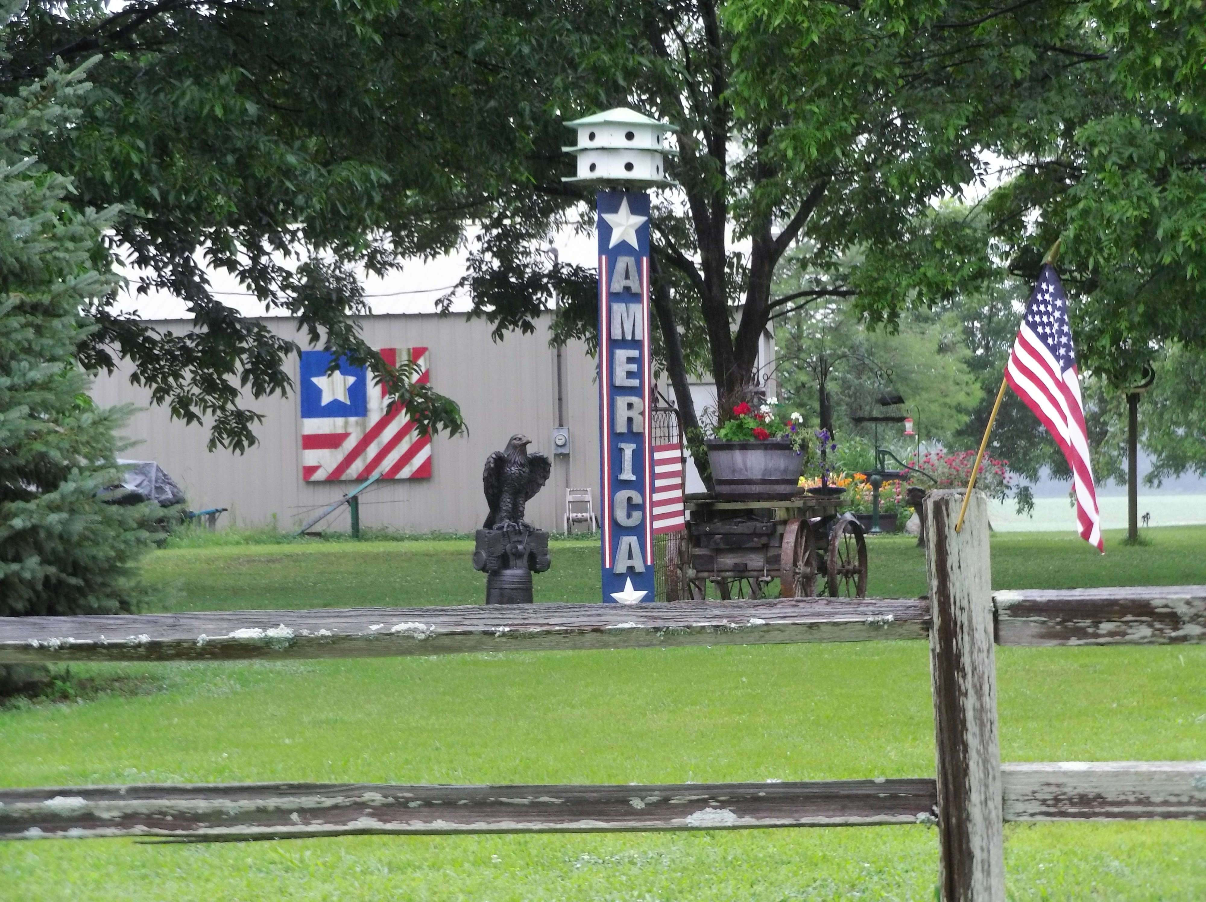 a fence, a statue of a bald eagle, many flags, and a big banner that says AMERICA, in a front yard