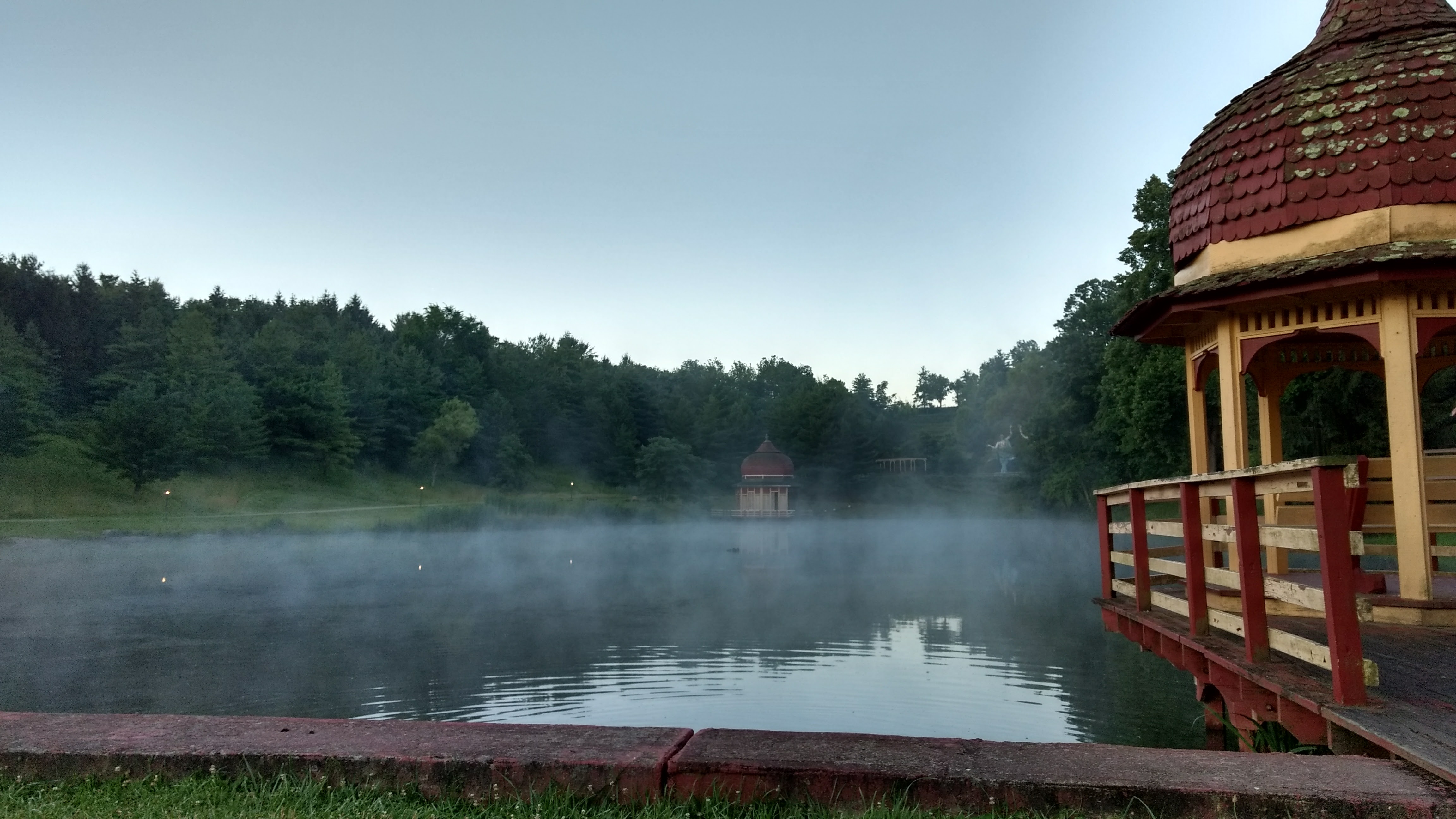 mist rising from a pond, red and yellow pavilions seen in background and foreground.